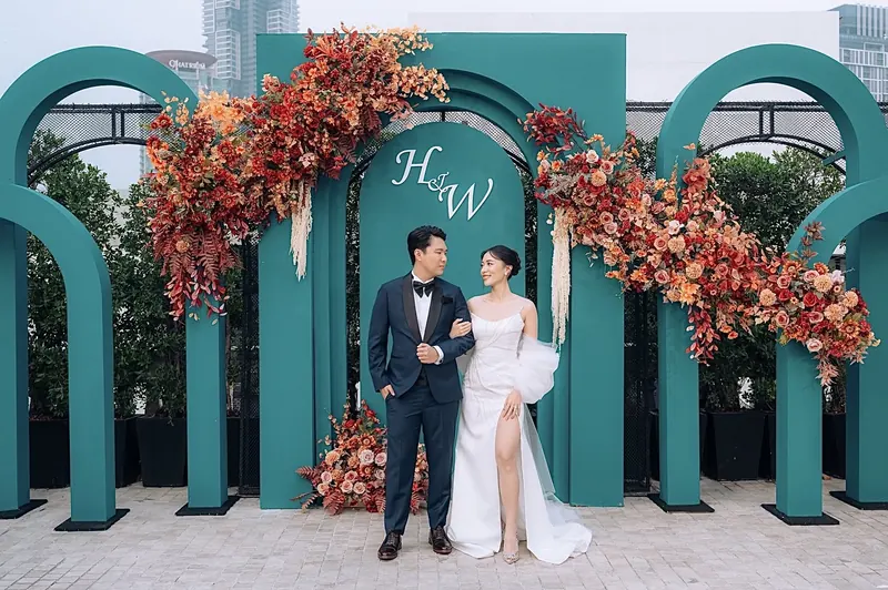 งานแต่งบนรูฟท็อป คู่บ่าวสาวหน้าซุ้มโค้งสีเขียวหัวเป็ดกับดอกไม้โทนส้มอิฐ
